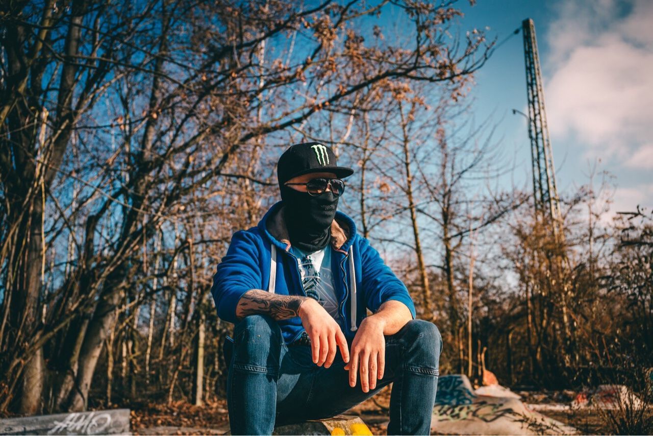 MAN SITTING ON BARE TREES AGAINST SKY