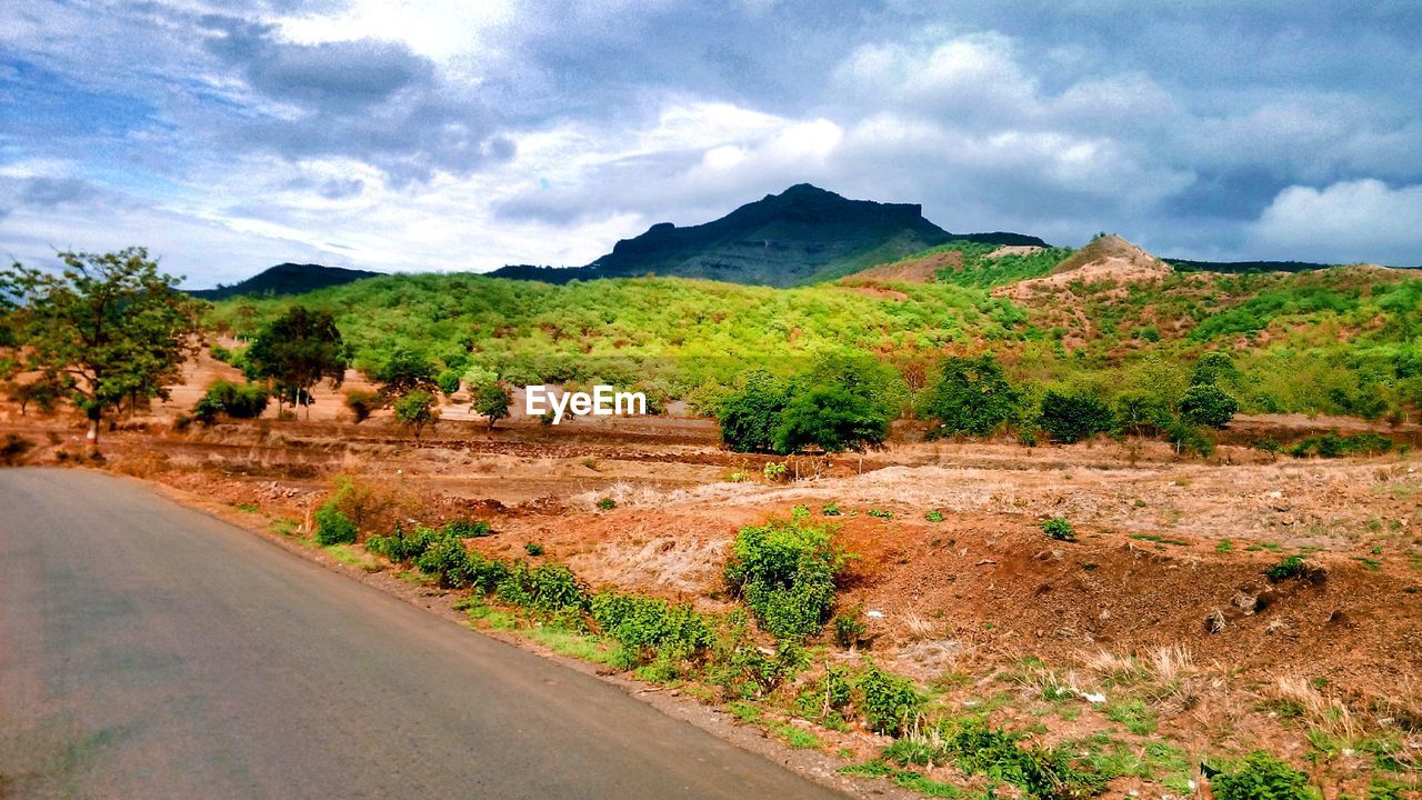 ROAD PASSING THROUGH MOUNTAINS AGAINST CLOUDY SKY