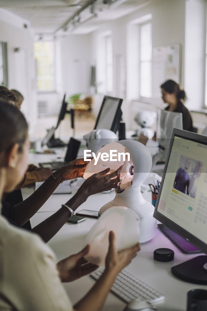 Multiracial students discussing over social robot at desk in innovation lab