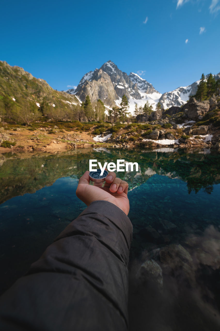 A man with a compass in his hand in the high mountains against the backdrop of a clear lake. travel