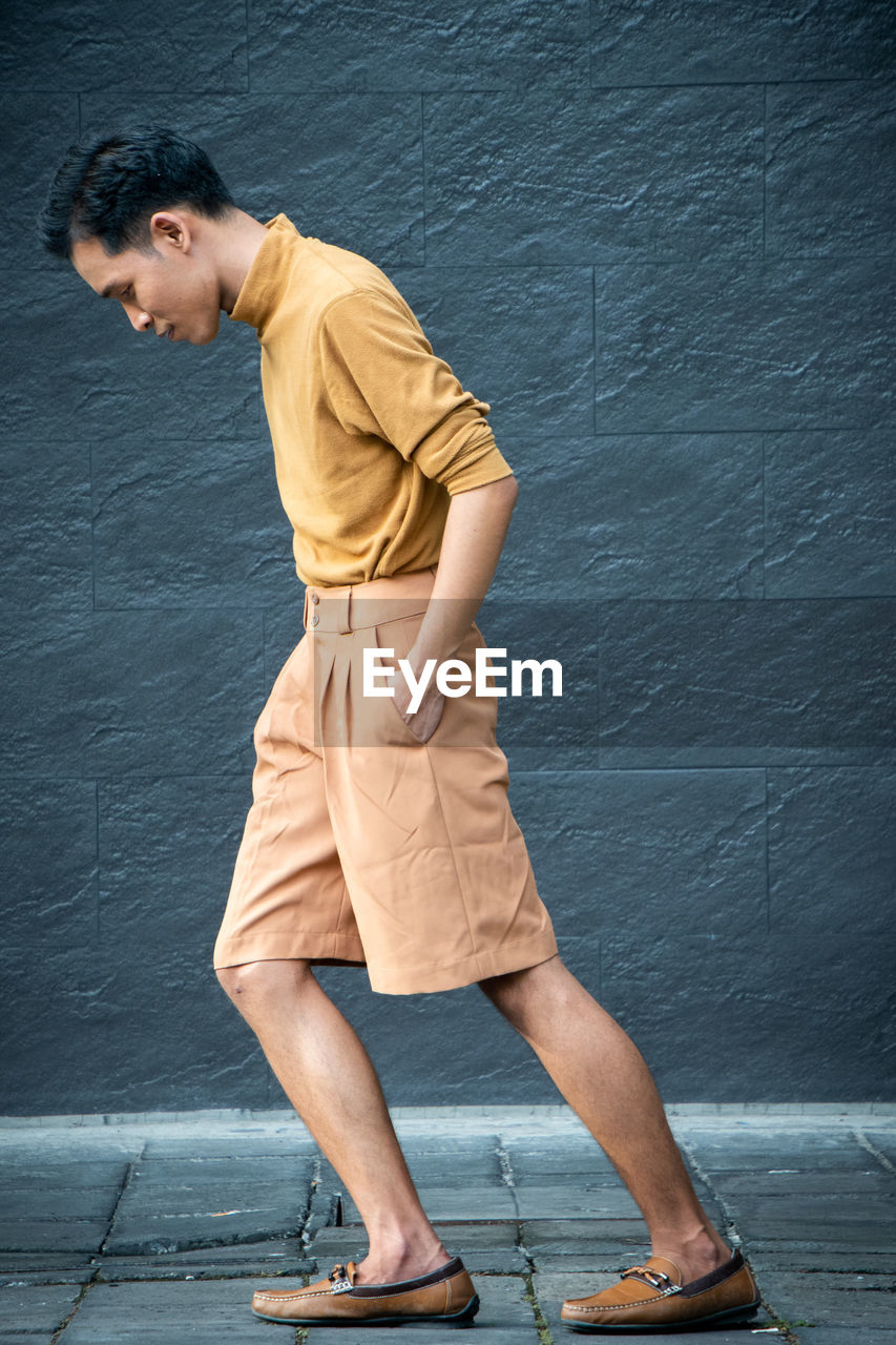 Side view of young man standing against wall