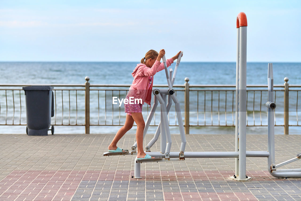 FULL LENGTH REAR VIEW OF WOMAN ON RAILING AGAINST SEA