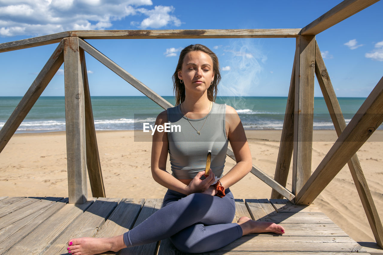 Woman meditating by the beach with a palo santo stick