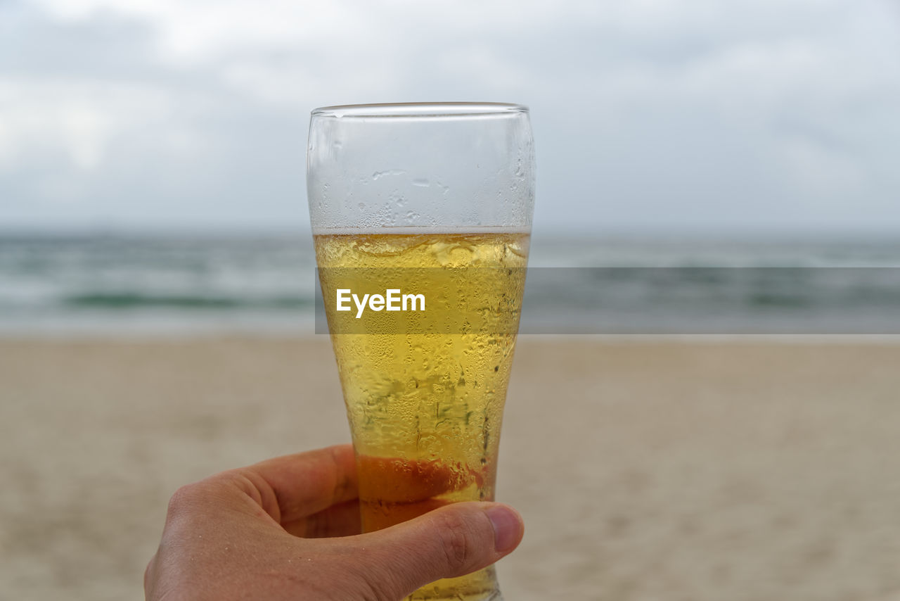 CLOSE-UP OF HAND HOLDING DRINK AT BEACH