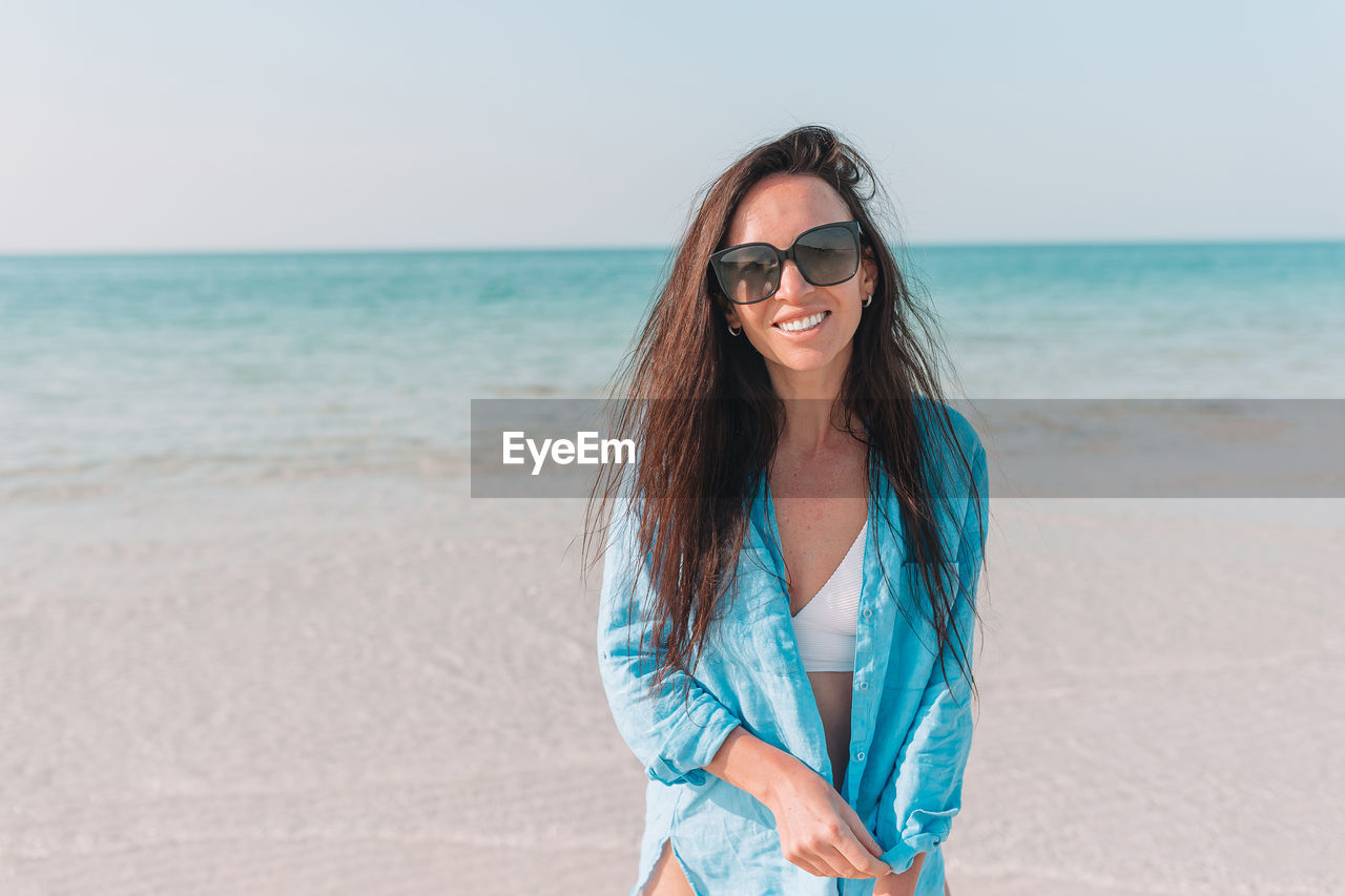 PORTRAIT OF YOUNG WOMAN WEARING SUNGLASSES AT BEACH