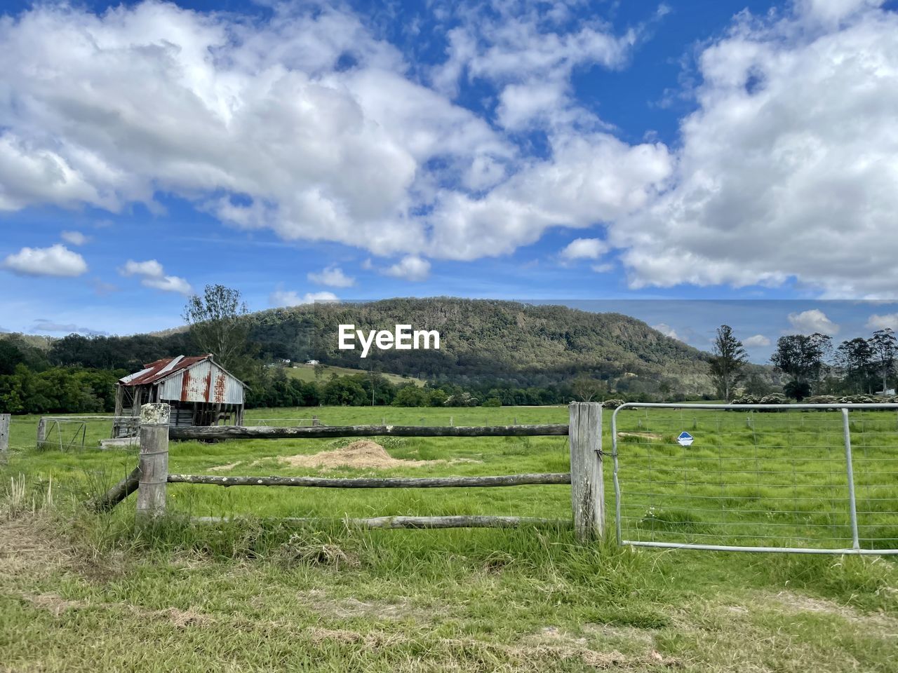 sky, cloud, landscape, plant, grass, land, fence, nature, environment, pasture, field, rural scene, rural area, scenics - nature, no people, farm, meadow, beauty in nature, architecture, mountain, tranquility, green, day, tranquil scene, tree, agriculture, outdoors, split-rail fence, built structure, non-urban scene, protection, security, gate, ranch, plain, building, wood, blue, grassland, prairie