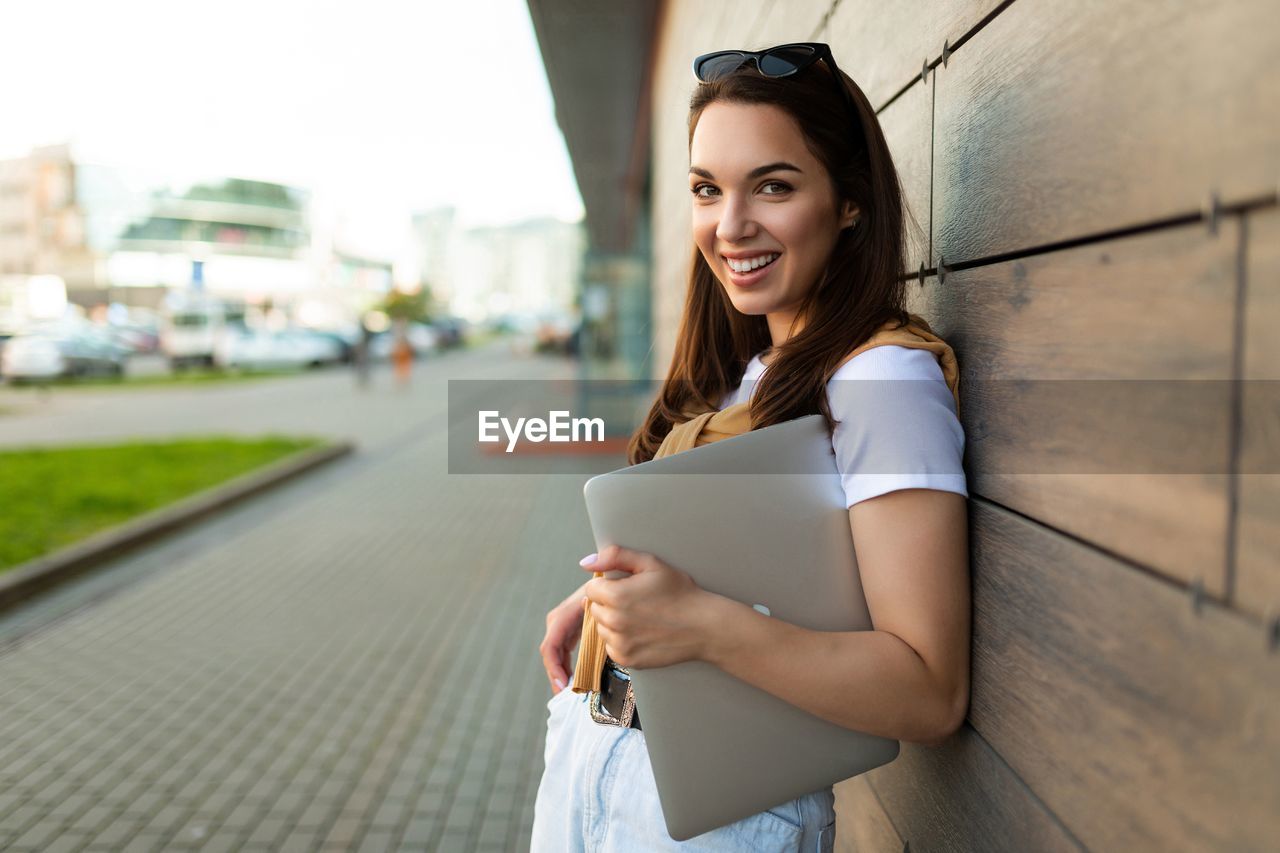 young woman using mobile phone while standing against wall