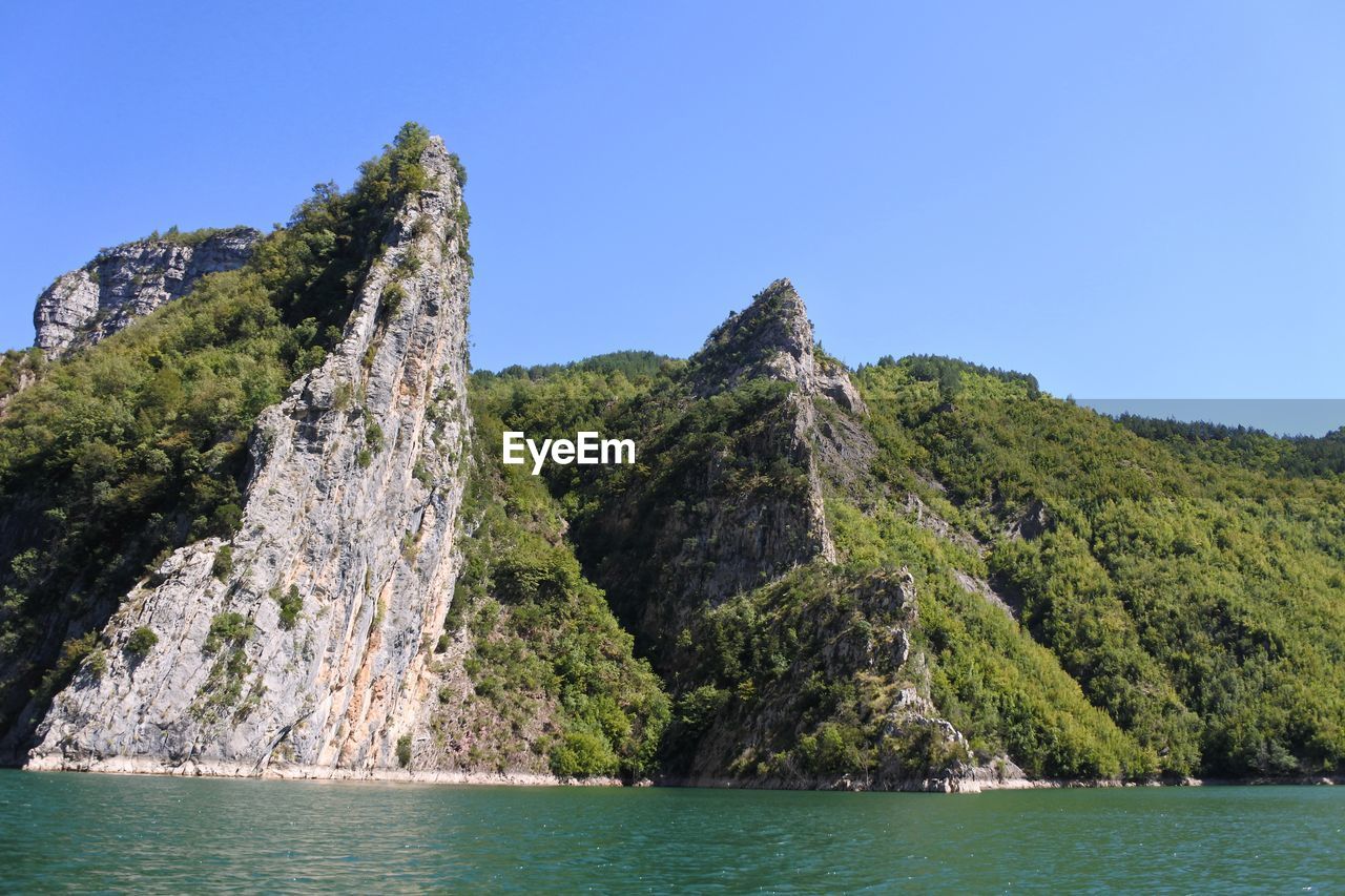 Scenic view of mountain by sea against clear sky