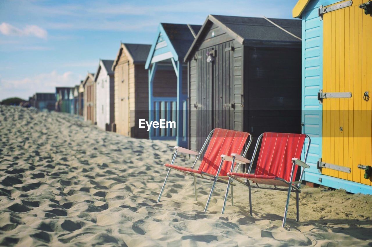 Empty chairs and huts at beach against sky