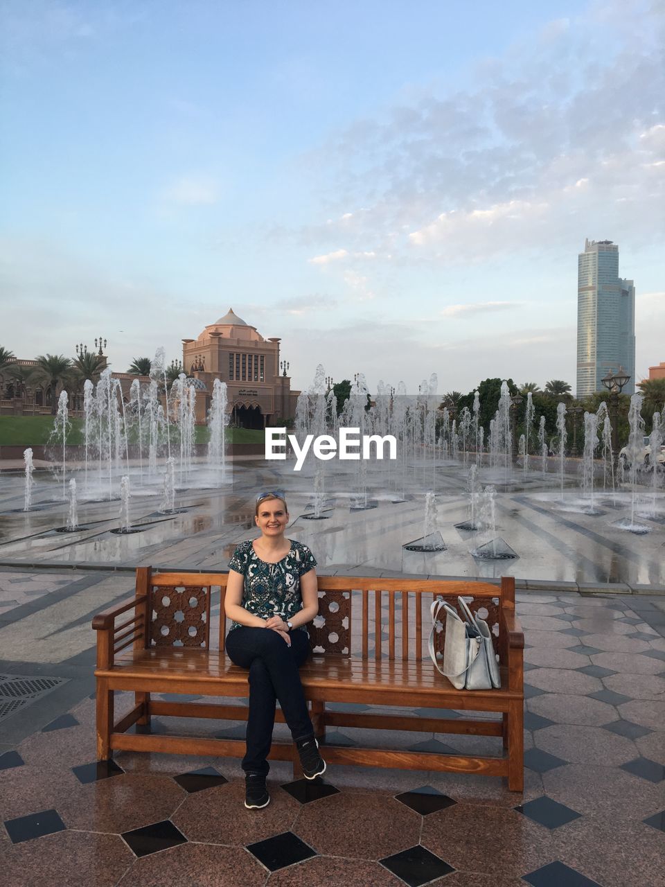 Portrait of smiling woman sitting on bench by fountain in city