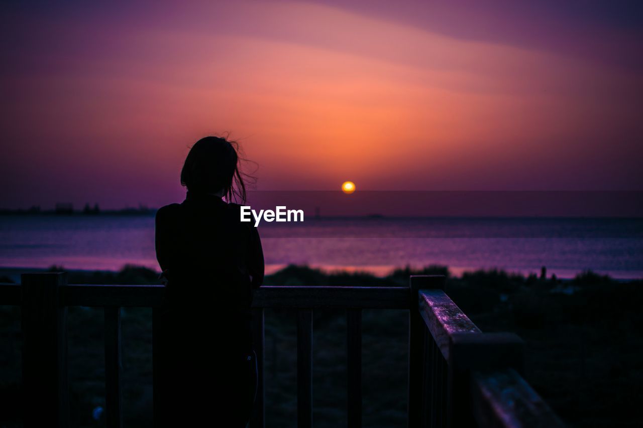 Rear view of silhouette woman looking at sea during sunset