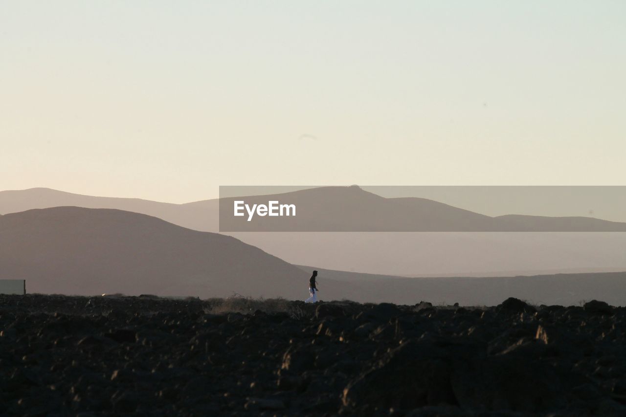 Distant view of man walking on mountain against sky