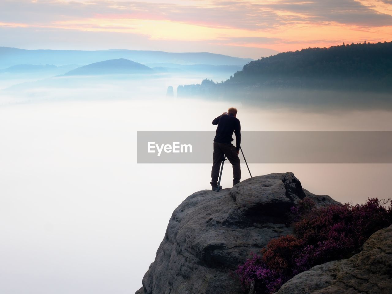 Professional photographer takes photos with mirror camera and tripod on peak of rock. misty  valley