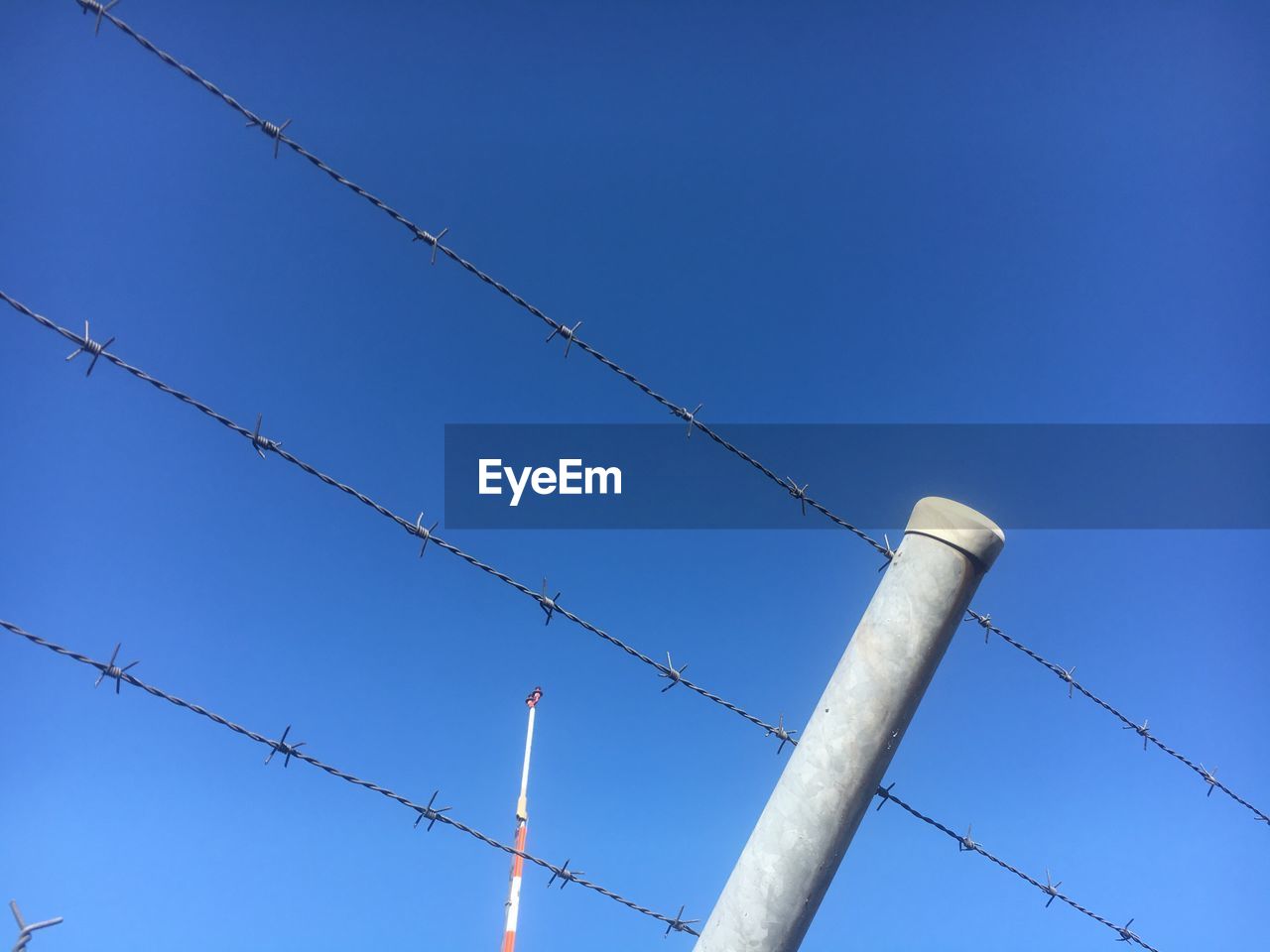 Low angle view of barbed wire fence against clear blue sky