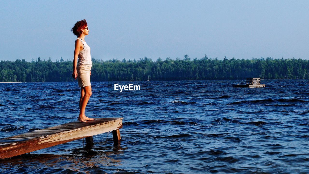 Woman standing on pier over lake against clear sky