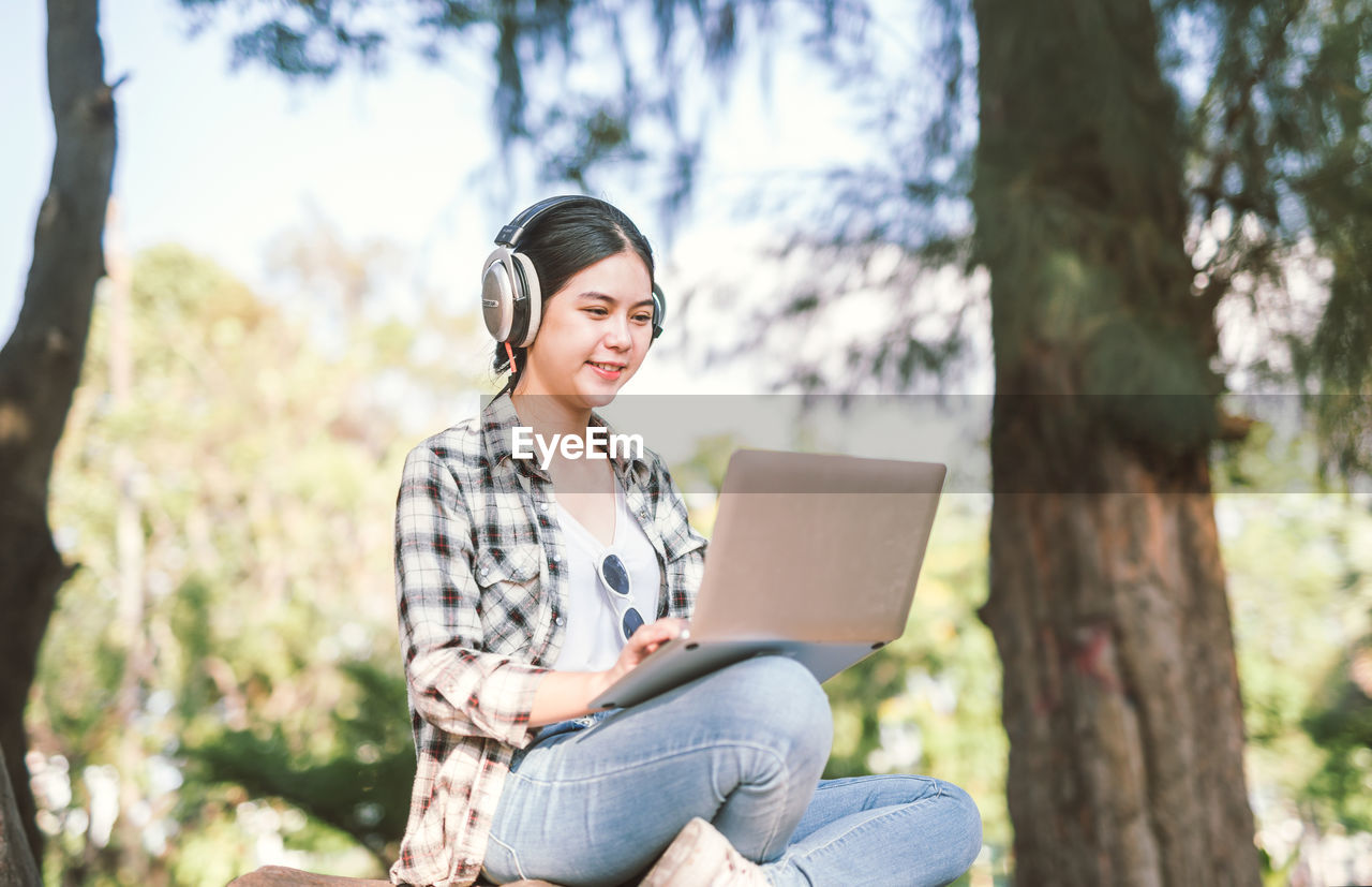 Young woman using laptop against trees