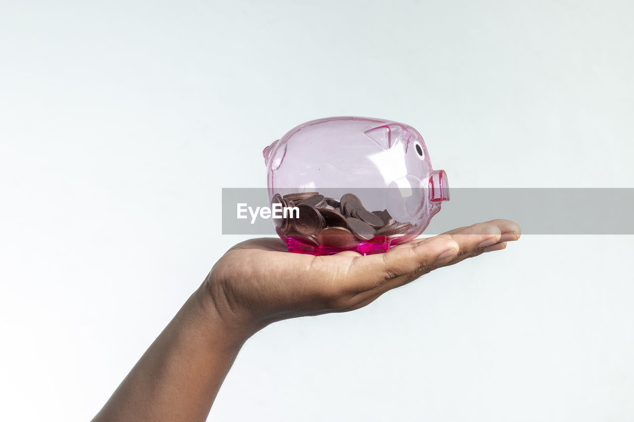 Cropped image of hand holding piggy bank against white background