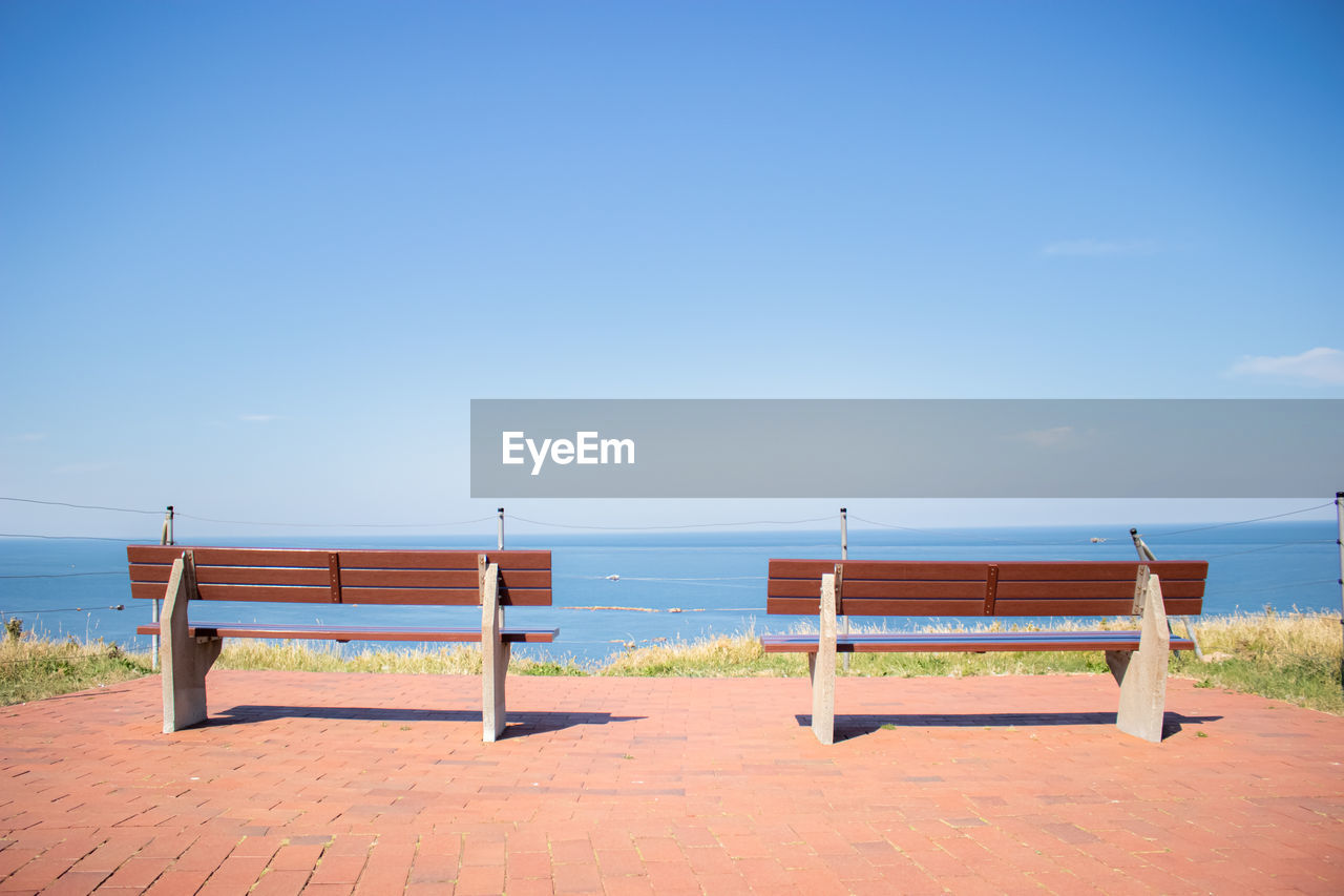 EMPTY BENCHES ON BEACH AGAINST SKY