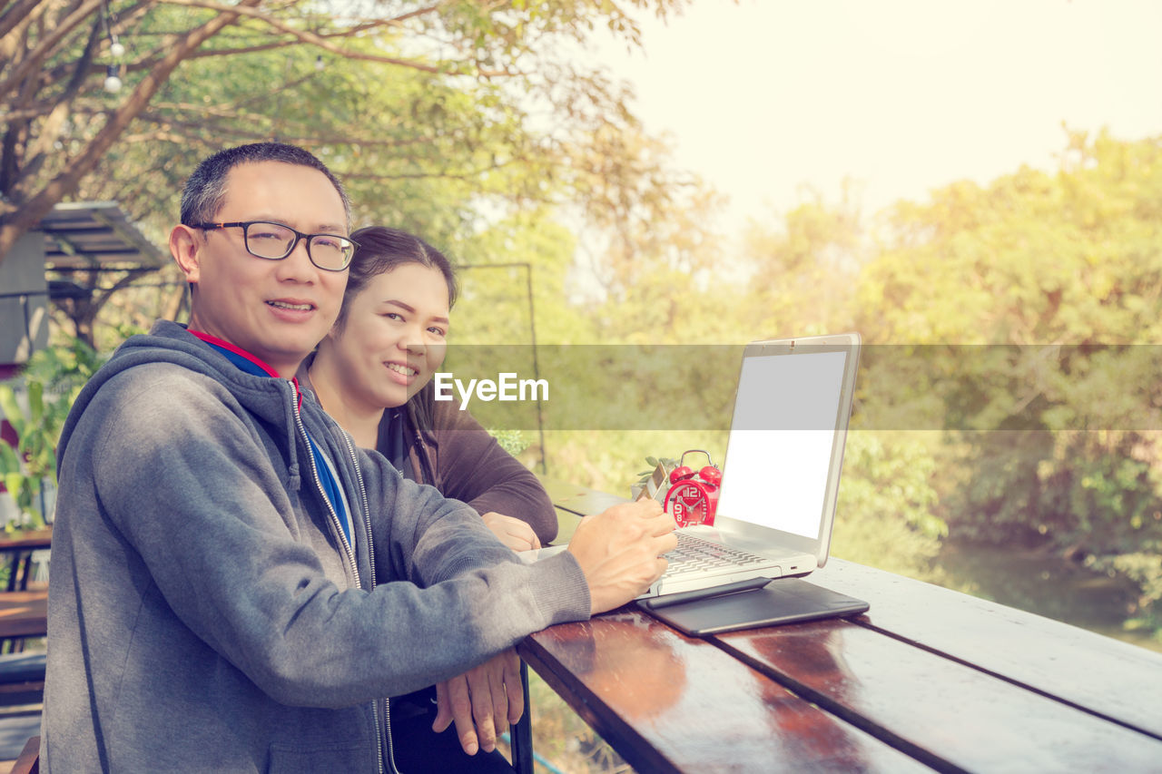 Portrait of smiling man and woman using laptop outdoors