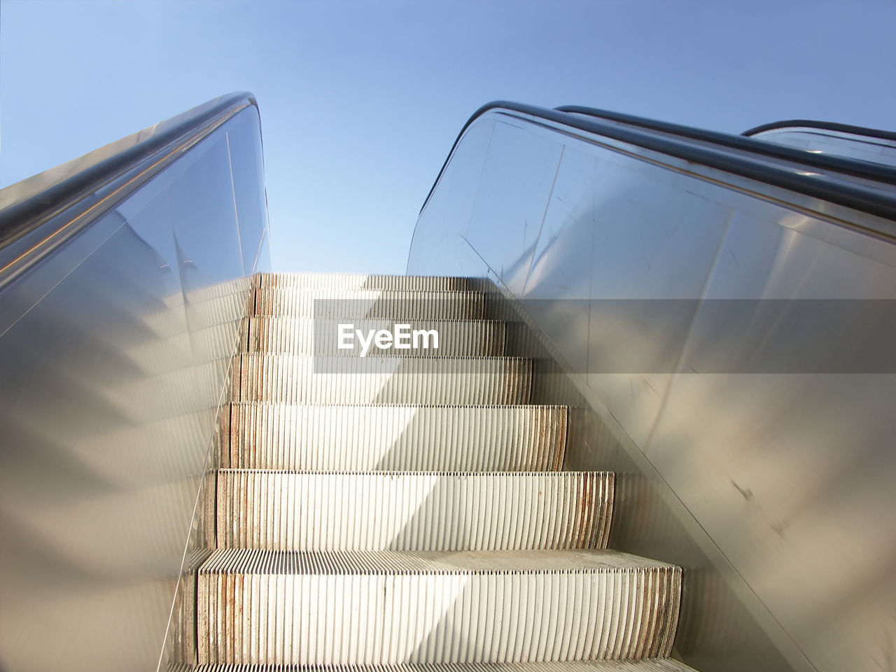 Closeup of exterior escalator viewed upwards with clear blue sky in the background