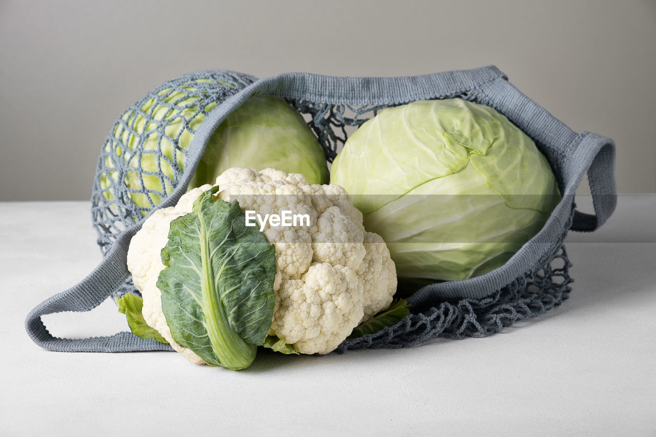 Heads of white cabbage and cauliflower lie on the surface in an eco-friendly mesh bag. 