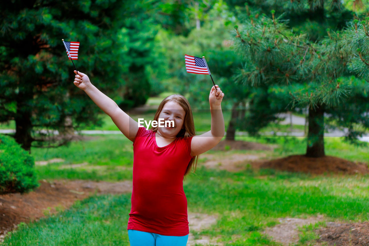 Cute overweight girl with small american flags standing at public park
