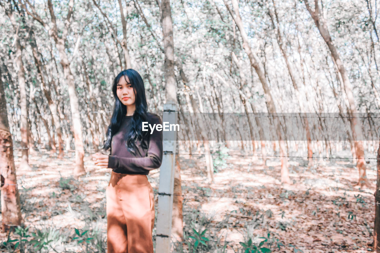 Portrait of young woman with long hair standing against trees in forest