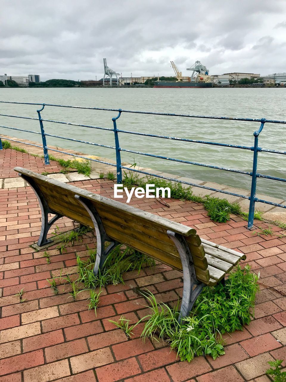 EMPTY BENCH IN PARK BY SEA AGAINST SKY