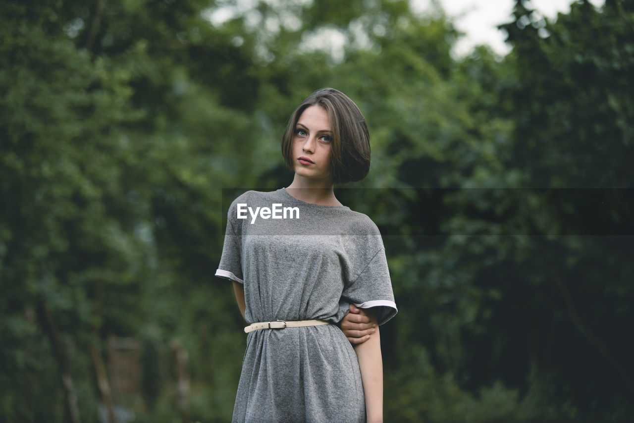 Portrait of beautiful young woman standing against trees