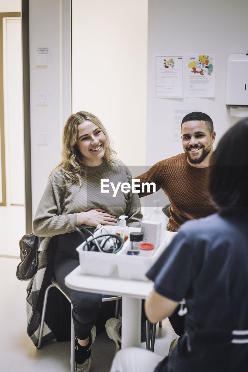 Rear view of female gynecologist discussing with pregnant woman sitting by man in medical clinic