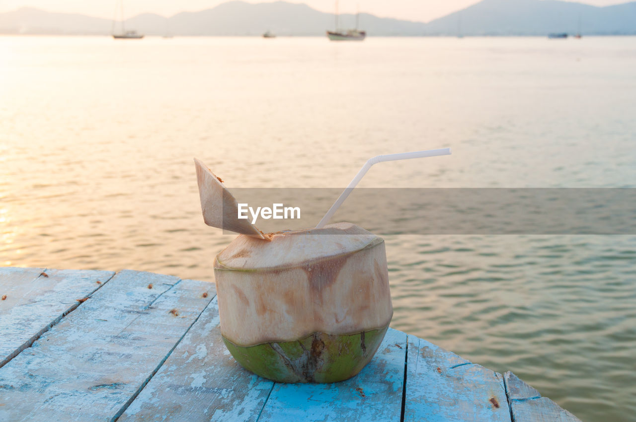 Close-up of coconut on table against sea during sunset