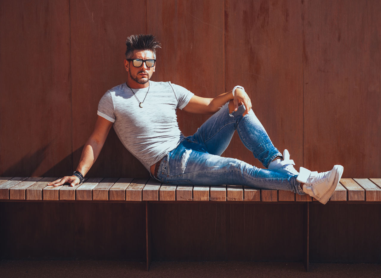 Handsome man wearing sunglasses while sitting against wall