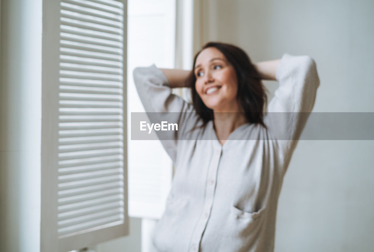 Portrait of young woman standing against window