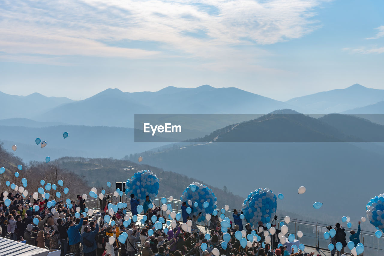 People with helium balloons against sky on sunny day