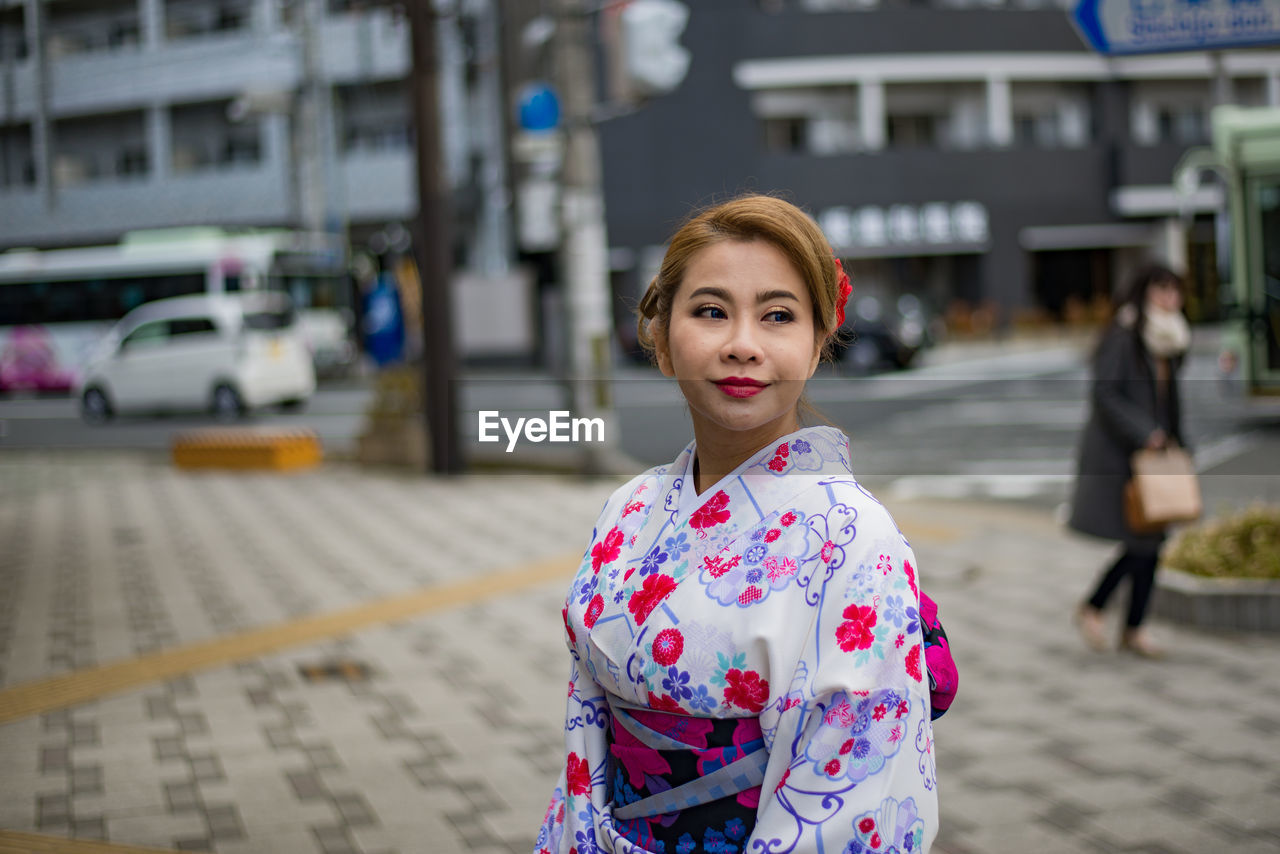 PORTRAIT OF SMILING YOUNG WOMAN ON STREET