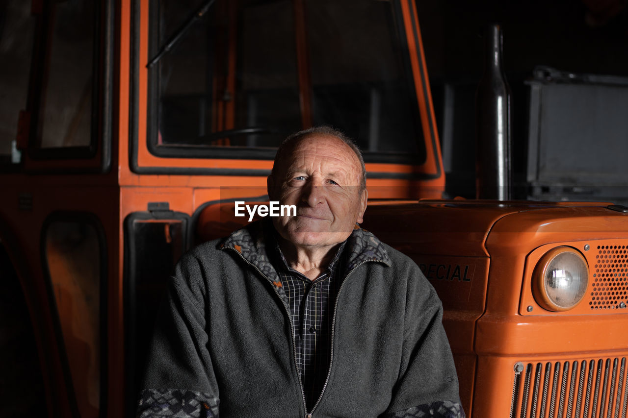 Portrait of senior man sitting by vehicle outdoors