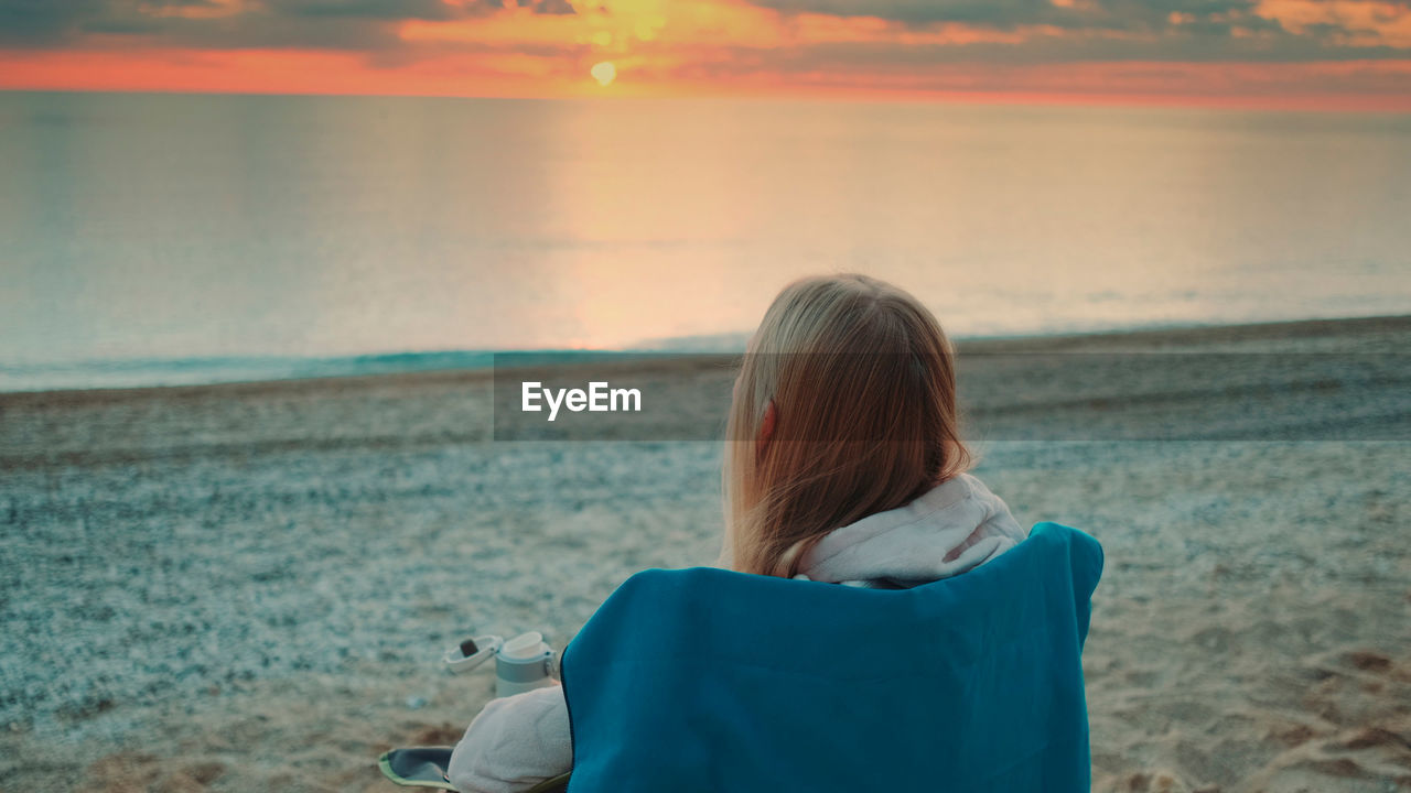 Rear view of woman looking at sea during sunset