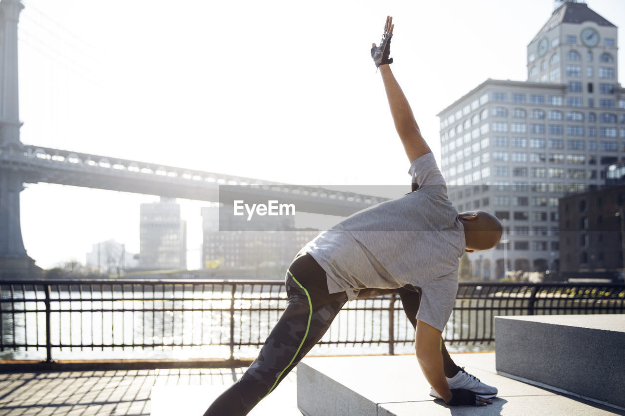 Male athlete exercising on promenade with manhattan bridge in background