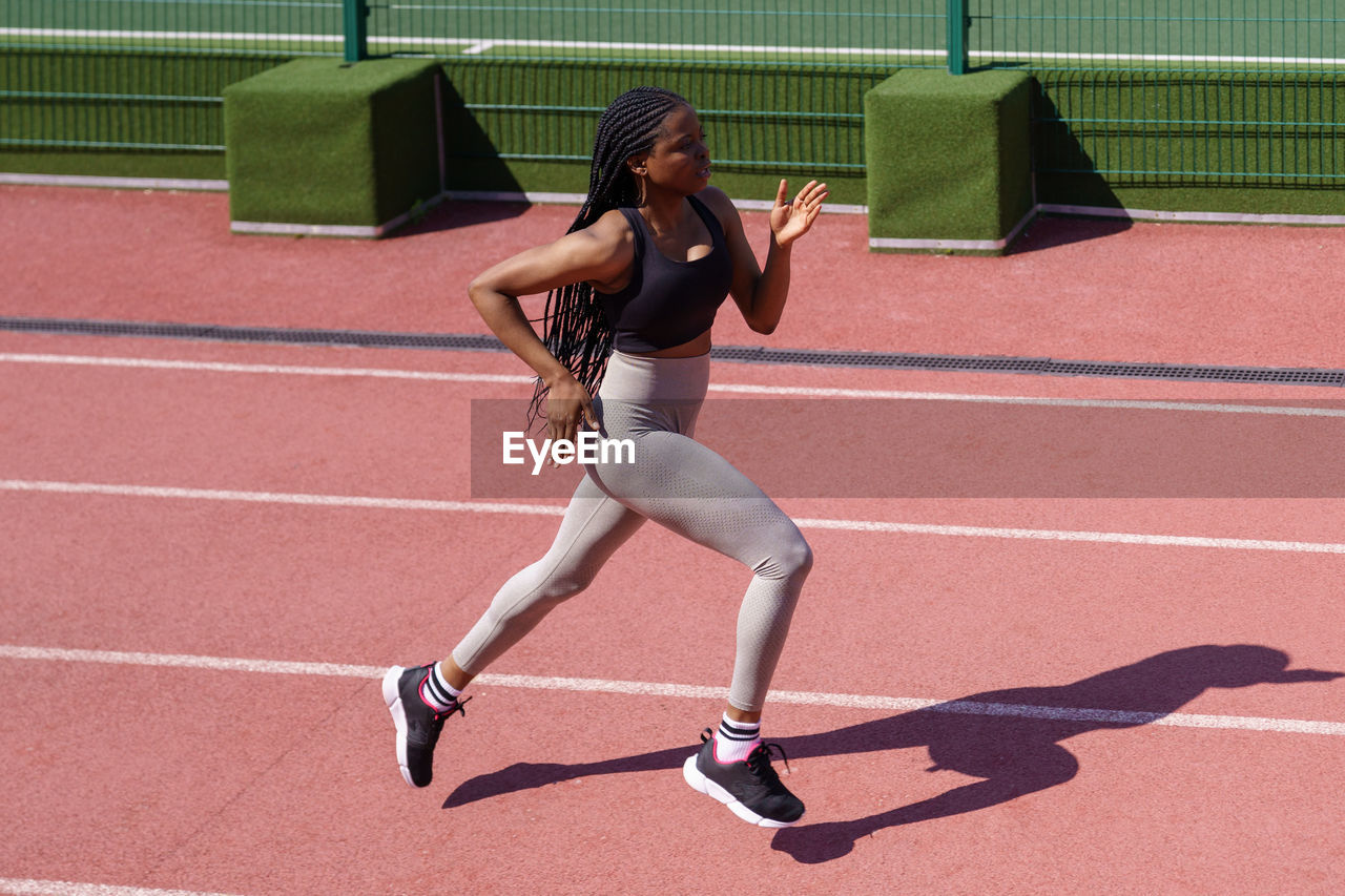 Young woman in headphones runs every day on red track at sports ground of big residential complex