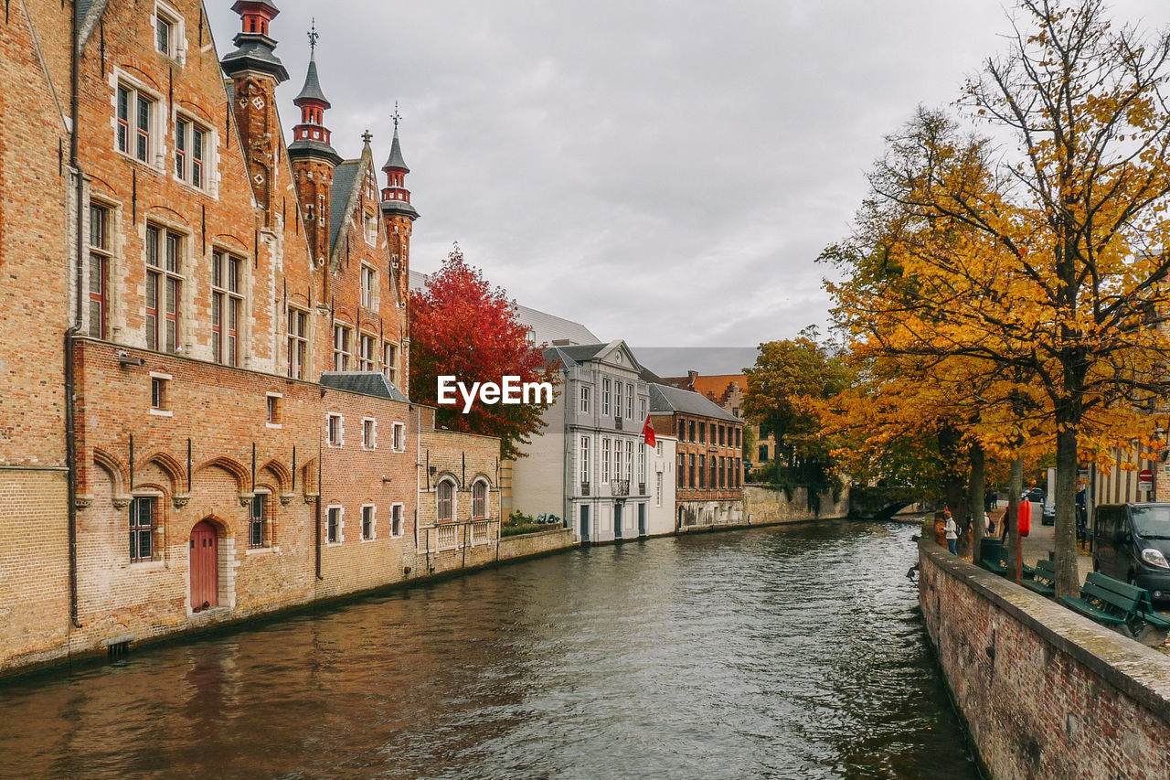 Canal by buildings against sky during autumn