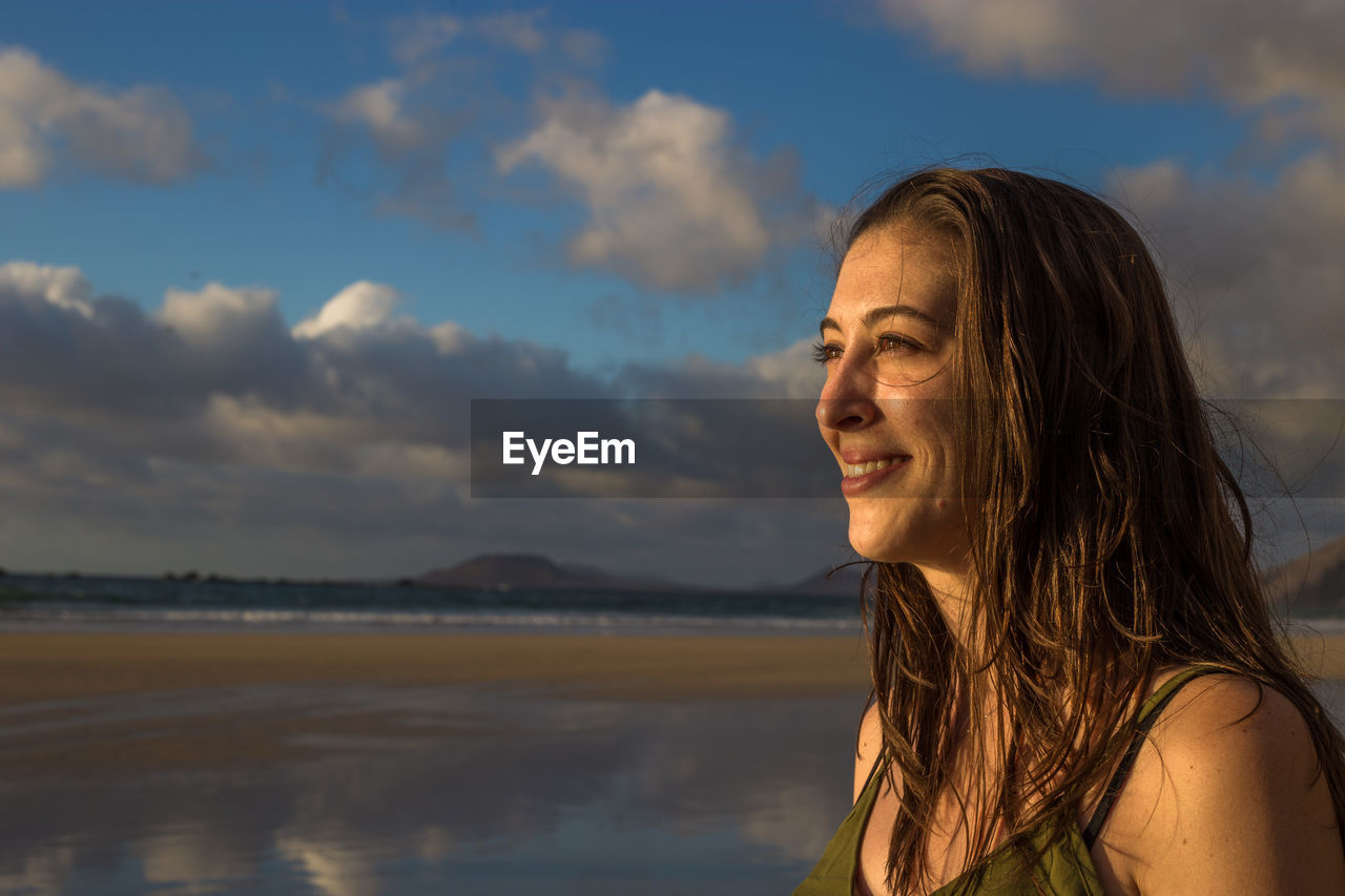 Portrait of smiling woman looking away against sky