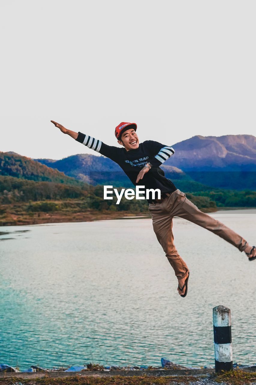 Full length of young man jumping against water 