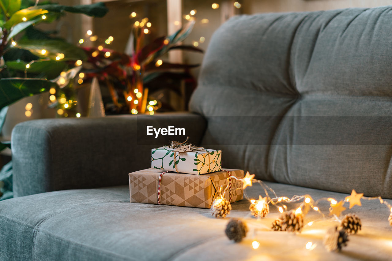 Christmas natural eco gift boxes on gray couch background at cozy home. glowing light bokeh, 