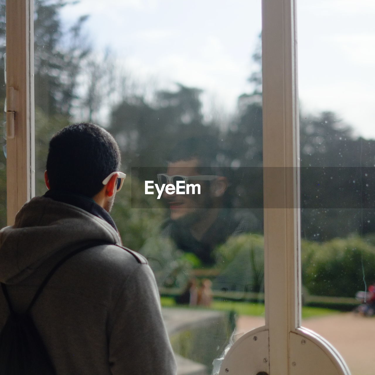 Rear view of man standing by window with reflection on glass