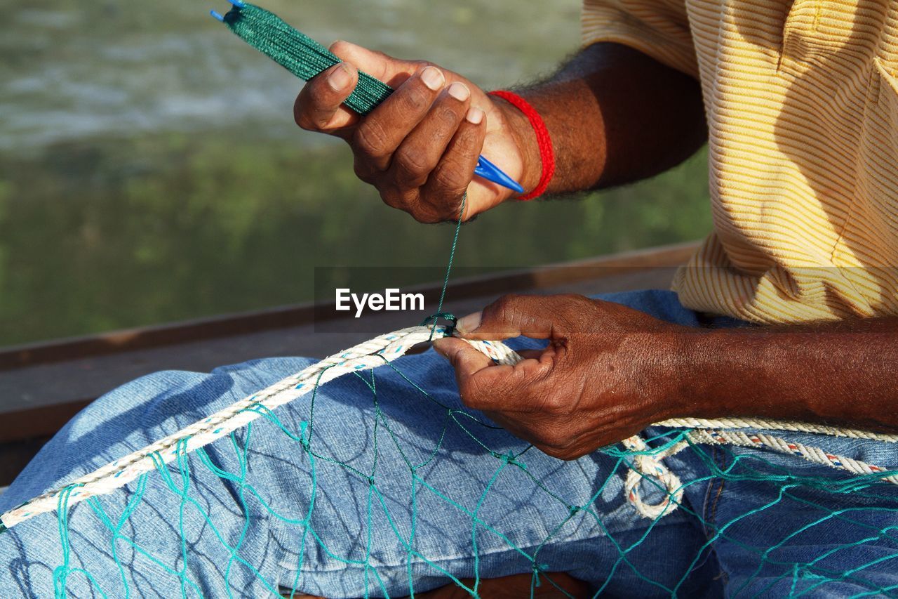 Mid section of a man stitching fishing net