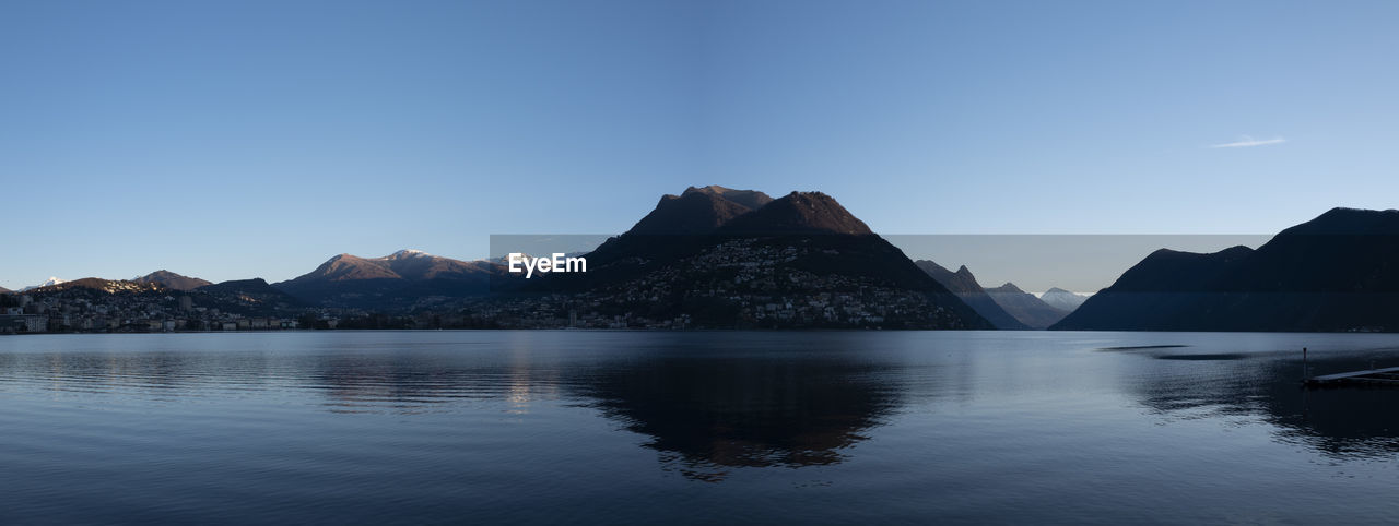 Scenic view of lake and mountains against clear blue sky