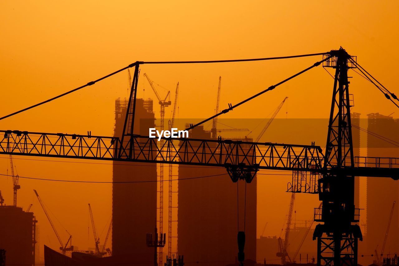 Silhouette crane at construction site against sky during sunset