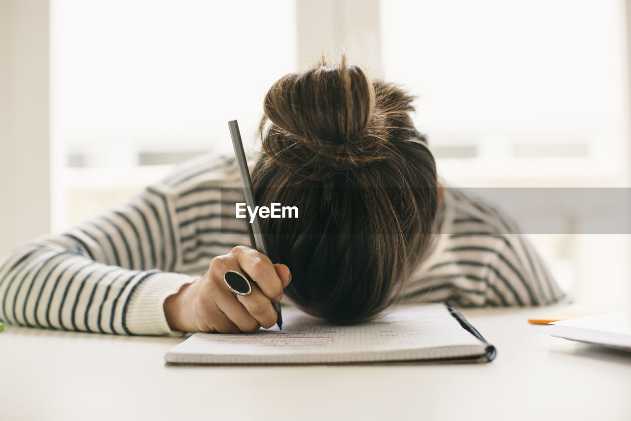 Woman writing on notepad resting her head on table