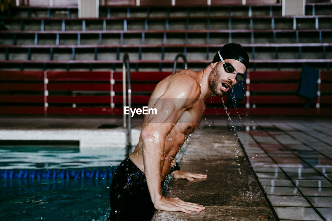 Shirtless young male swimmer leaning on poolside