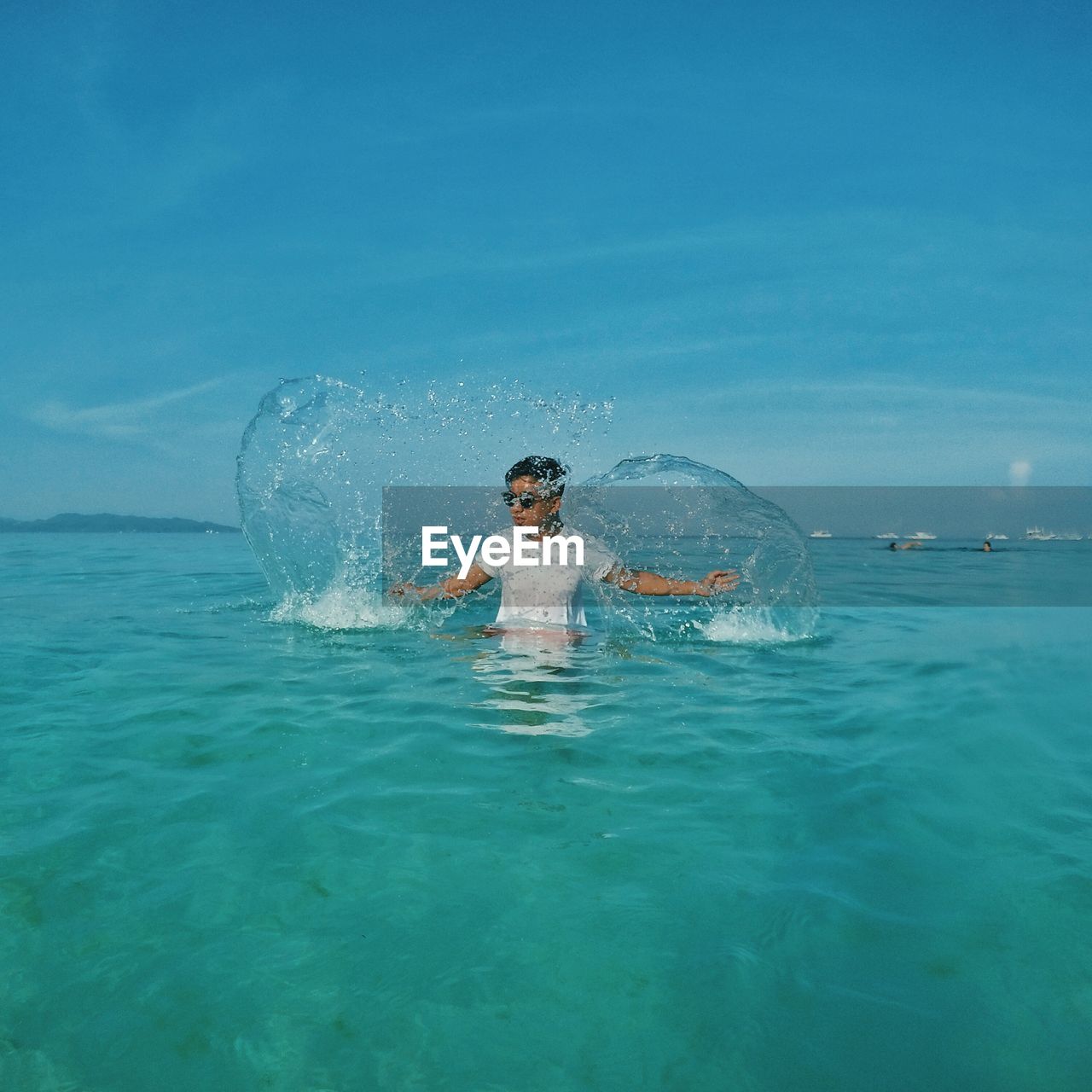 Playful teenage boy in sea against blue sky